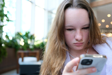 young girl with freckles a European woman sits with a phone in her hands in the lobby of a hotel....