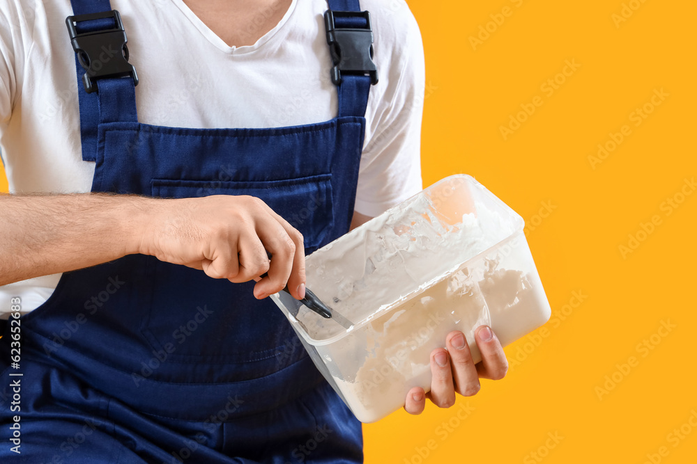 Wall mural male decorator with putty knife and plaster on yellow background, closeup