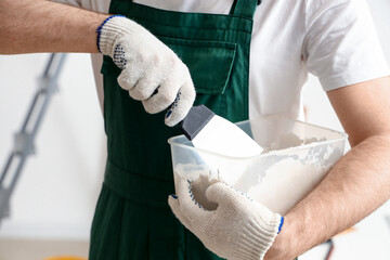Male decorator with putty knife and plaster working in room, closeup