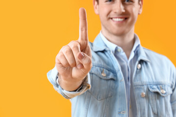 Young man using virtual screen on yellow background, closeup