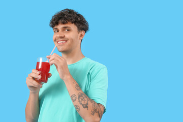 Young man with glass of red juice on blue background