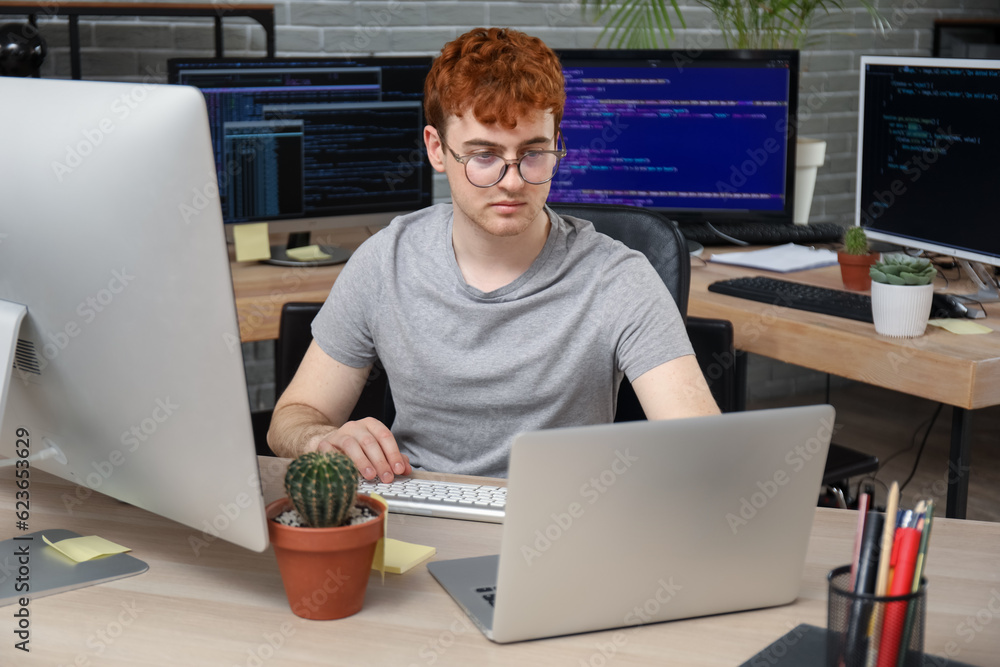 Poster male programmer working with laptop at table in office