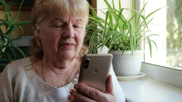 Smiling elderly woman with smartphone having video call at home. Technology, gadget and old people