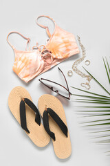 Stylish bikini top, flip-flops, sunglasses, accessories and palm leaf on light background