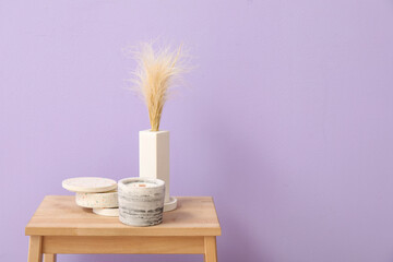 Holders with candles and pampas grass on wooden table near purple wall in room