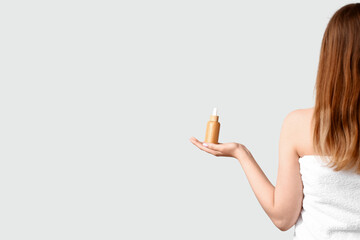 Young woman with cosmetic oil for hair treatment on light background, back view