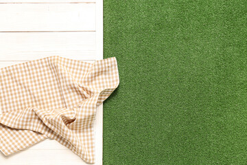 Clean napkin on light wooden table against green grass background