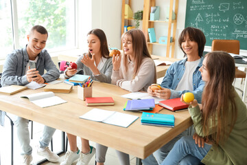 Group of teenage students having snacks at table in classroom