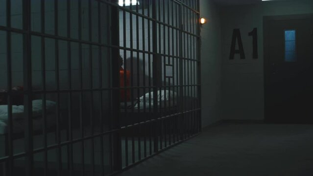 Guilty criminals in orange uniforms lay and sit on the beds in prison cells. Two prisoners serve imprisonment terms for crimes in jail. Depressed inmate in detention center or correctional facility.