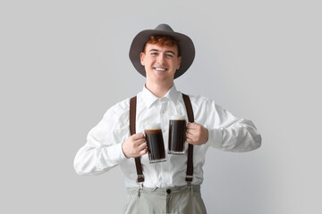 Young man in traditional German clothes with beer on light background