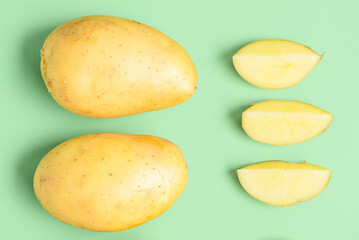 Whole and cut potatoes on green background