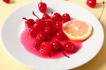 Plate of tasty maraschino cherries and lemon on yellow background