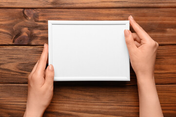 Woman holding blank photo frame on wooden background