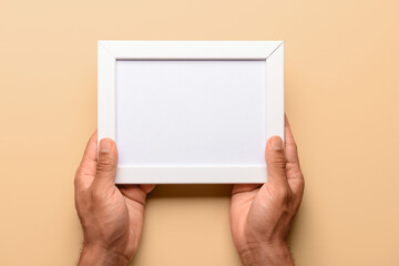 Man holding blank photo frame on beige background