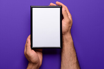 Man holding blank photo frame on purple background