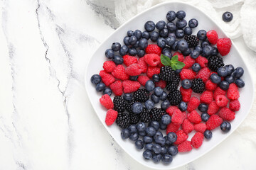 Plate with fresh berries on light background