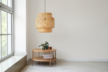Wooden coffee table with houseplant and wicker lamp near white wall