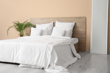 Comfortable bed with white pillows, mirror and houseplant in bedroom