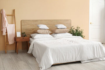 Comfortable bed with white pillows, bedside table and houseplant in bedroom - Powered by Adobe