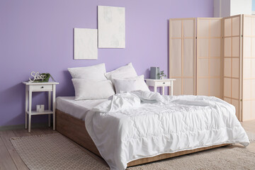 Interior of stylish bedroom with comfortable bed, white pillows, bedside tables and folding screen