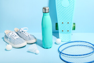 Bottle of water, sports equipment and shoes on color background
