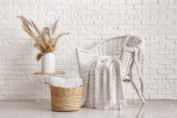 Rattan armchair with knitted plaid and wicker basket with cushion near white brick wall