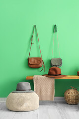 Wooden bench with wicker basket, hats and purses near green wall