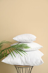 Fototapeta na wymiar Table with white pillows and houseplant near beige wall