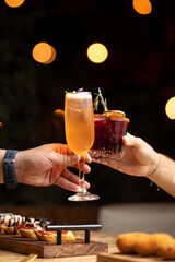 Toasting in a restaurant with two cocktails, at a table with dishes. With a dark background with beautiful lights