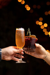 toasting with two cocktails, in a dark background with lights