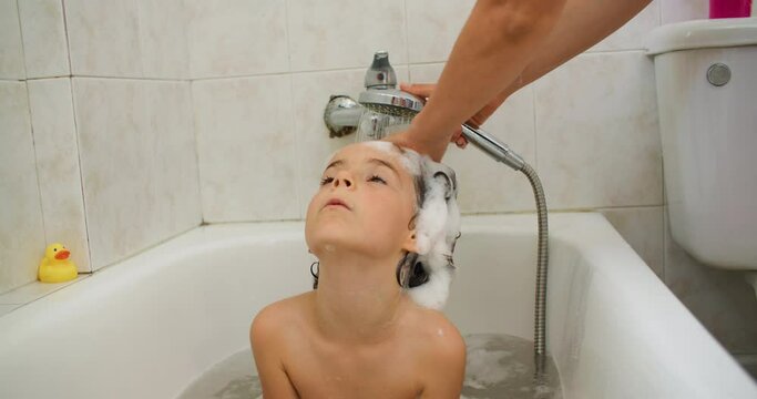 A mother washes her daughter's hair in the shower. A woman lathers shampoo on a child's head. Girl bathing in the bath. High quality 4k footage
