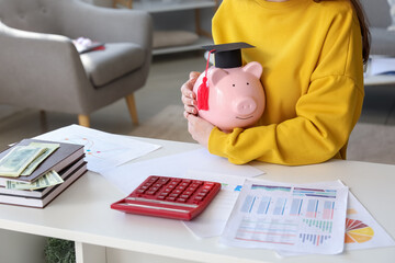 Female student holding piggy bank in graduation cap. Student loan concept