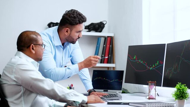 Indian trader explaining about stock market strategy from candle stick charts and financial papers to colleague at office - concept of Investment advicer, teamwork and coordination