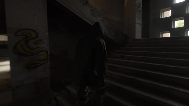 A young man in protective clothing and a respirator climbs a dark staircase in an old building