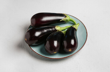 Plate with fresh eggplants on light background