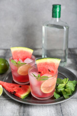 Glasses of tasty watermelon cocktail with lime and mint on grunge grey table near wall