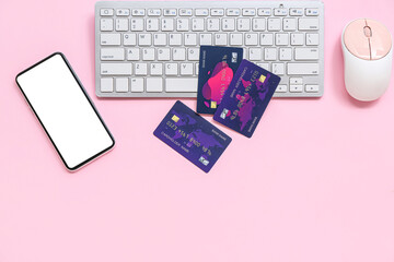 Keyboard with credit cards, computer mouse and mobile phone on pink background