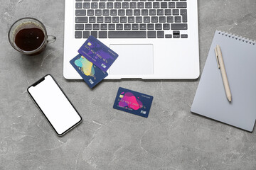 Laptop with credit cards, mobile phone and cup of coffee on grunge grey background