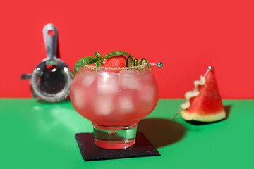 Glass of tasty watermelon cocktail with strainer on green table near red wall