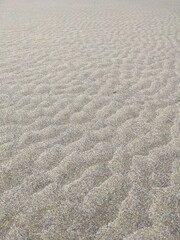 Angled view of beach sand with periodic pattern from the ebb and flow of water.