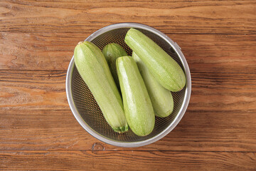 Colander with fresh green zucchini on wooden background
