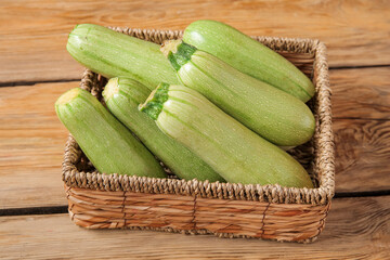 Wicker box with fresh green zucchini on wooden background