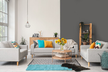 Cozy grey sofas and vase with beautiful sunflowers in interior of light living room