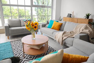 Cozy grey sofas and vase with beautiful sunflowers in interior of light living room