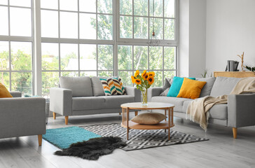 Cozy grey sofas and vase with beautiful sunflowers in interior of light living room - obrazy, fototapety, plakaty