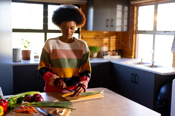 Happy african american woman preparing meal chopping vegetables in sunny kitchen, copy space