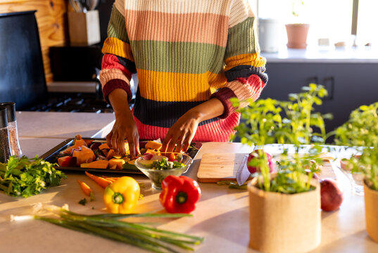 Midsection of african american woman preparing meal in kitchen arranging vegetables on baking tray