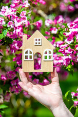 The girl holds in her hand the symbol of the house against the background of blooming weigela
