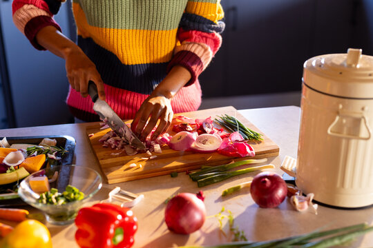 Midsection of african american woman preparing meal chopping vegetables in sunny kitchen