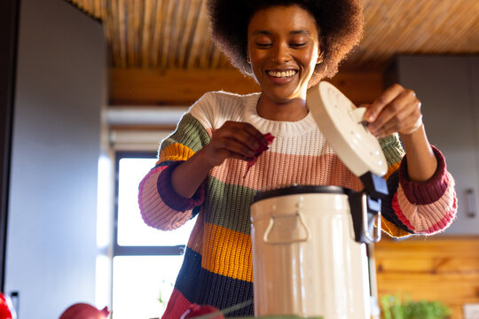 Happy african american woman preparing meal composting vegetable waste in sunny kitchen